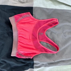 Rosa sport-bh från Decathlon - Säljer en sportig rosa sport-bh från Decathlon med bred resår och brottarrygg. Perfekt för träning och har en tight passform. Materialet är syntet och bh:n har en diskret logga på resåren.