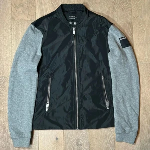 Replay Cardigan - Snygg Replay Cardigan med svarta paneler i kroppen och gråa ärmar. Jackan är perfekt inför våren och lite kyligare sommardagar