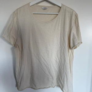Beige t-shirt från East West - En enkel och stilren beige t-shirt från East West. T-shirten har rund halsringning och korta ärmar. Perfekt basplagg i garderoben och lätt att matcha med andra kläder. Perfekt sommarplagg.