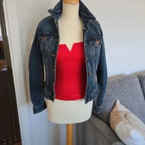 Klassisk jeansjacka från H&M - Säljer en klassisk blå jeansjacka från H&M med bruna knappar och två bröstfickor. Jackan har en figurnära passform och är tillverkad i denim med snygga sömdetaljer. Perfekt att slänga över en t-shirt eller topp.