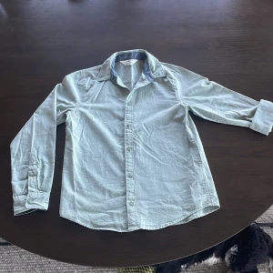 Ljusgrön skjorta med krage - Säljer en ljusgrön skjorta med lång ärm och klassisk krage. Skjortan har knappar framtill och en snygg kontrastdetalj på insidan av kragen. Perfekt för dig som vill ha en stilren och enkel look.