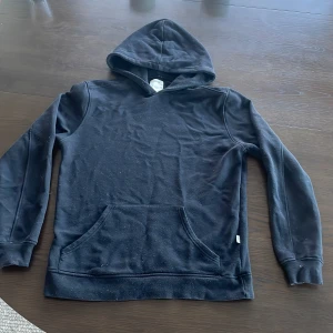 Svart hoodie med ficka - En klassisk svart hoodie med huva och magficka. Tröjan har långa ärmar och är tillverkad i mjukt material, perfekt för en avslappnad stil. Passar både till jeans och mjukisbyxor. DEN ÄR NOPPIG!