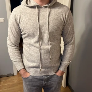 Ljusgrå cardigan i 100%  kashmir - Mjuk och stilren ljusgrå kashmir cardigan med dragsko i huvan. Tröjan har långa ärmar och ribbade muddar vid ärmslut och nederkant. 100% Kashmir. Aldrig använt goodie bag finns med. Storlek M, pris går att diskutera 