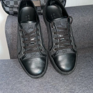 Svarta sneakers från Gucci - Säljer ett par svarta sneakers från Gucci med klassiskt GG-mönster i textil och detaljer i skinn. Skorna har svarta snören, rund tå och platt sula. Perfekta för dig som gillar stilrena och lyxiga sneakers. Använda fåtal gånger passar även 42 ,priset är ej hugget i sten vid snabb affär 🌟!