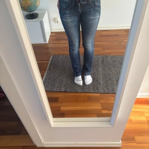 Blå jeansbyxor från Fornarina - Säljer ett par klassiska blå jeans från Fornarina med snygga slitningar och kontrastsömmar. Byxorna har normal passform och raka ben, samt fem fickor och låg midja. Perfekta till en avslappnad stil.
