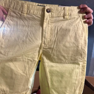 Ljusgula shorts med knapp och fickor - Snygga ljusgula shorts med klassisk passform, knapp och dragkedja i midjan samt sidofickor. Perfekta för varma dagar och enkla att matcha med olika toppar.