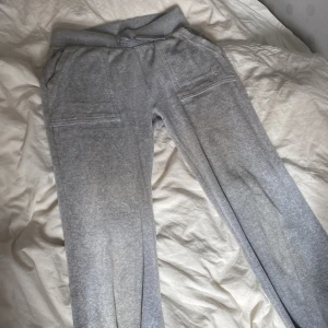 Grå mjukisbyxor Juicy Couture XXS - Supermysiga grå mjukisbyxor från Juicy Couture i storlek XXS. Byxorna har bred resår i midjan med snörning, stora fickor fram och bak med snygga silverknappar med logga. Perfekta för chill eller när du vill vara bekväm men ändå se snygg ut.