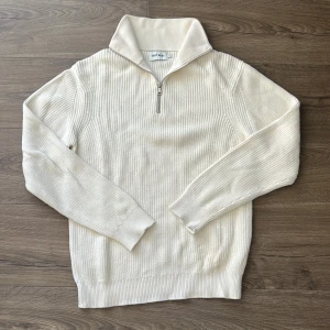 Vit ribbstickad half zip-tröja East West - Snygg vit ribbstickad tröja från East West i 100% bomull. Tröjan har hög krage och half zip-dragkedja framtill. Långärmad modell med klassisk passform, perfekt för lager-på-lager och chill stil. Nästan aldrig använd