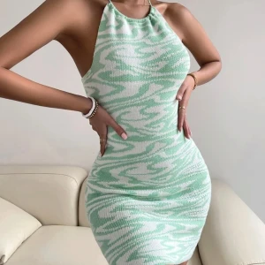 Mintgrön stickad kortklänning med mönster - Superfin mintgrön och vit stickad kortklänning med halterneck och tajt passform. Klänningen har ett coolt abstrakt mönster och är ärmlös med öppen rygg. Perfekt för dig som vill sticka ut med en fräsch och trendig look!