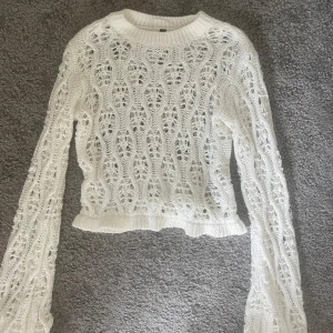 Vit stickad croppad  - Säljer en vit stickad tröja i croppad modell med lång ärm. Tröjan har ett genombrutet, virkat mönster och ribbade muddar vid hals, ärmslut och nederkant. 
