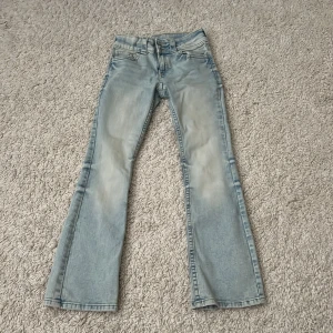 Ljusblå bootcut jeans med dubbla knappar - Snygga ljusblå jeans med bootcut passform och dubbla knappar i midjan. Jeansen har slitna detaljer, klassiska fickor fram och bak med lock och knapp.