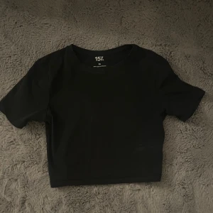 Svart croppad topp från lager 157 - Enkel och stilren svart croppad topp från lager 157. T-shirten har rund halsringning och korta ärmar, perfekt att matcha med höga jeans eller kjol. Tillverkad i mjuk bomull med lite stretch för en bekväm passform.