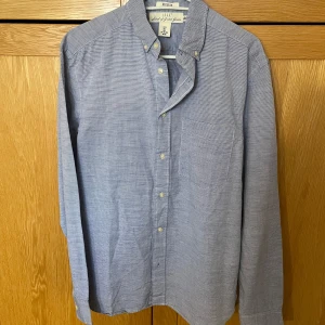 Blå randig skjorta från L.O.G.G. - Säljer en stilren blå skjorta från L.O.G.G. med diskreta ränder, klassisk button-down krage och bröstficka. Skjortan är långärmad och har knappar framtill. Perfekt för dig som gillar en clean och enkel look.