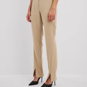 Beige och svarta kostymbyxor NA-KD - Två par stilrena kostymbyxor från NA-KD i färgerna beige och svart. Byxorna har raka ben med slits framtill, hög midja och stängs med dragkedja och knapp. Perfekta för en clean och trendig look. Materialet är mjukt och följsamt.