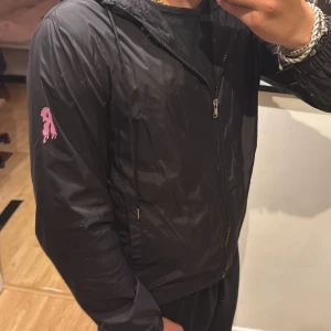 Svart risky vindjacka - Svart vindjacka från Risky med huva och dragkedja framtill. Jag säljer jackan då den inte alls var min stil efter jag fick den och den är helt oanvänt med tagsen kvar på den. Skriv vid funderingar och annat