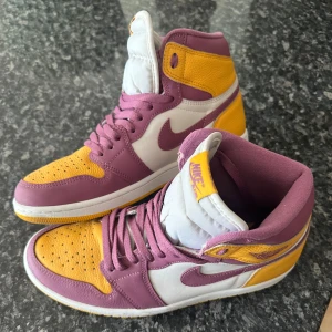 Nike Air Jordan 1 High lila/gul - Säljer ett par Nike Air Jordan 1 High med en snygg färgkombo i lila, gul och vitt. Skorna har klassisk snörning, hög siluett och är gjorda i skinn med perforerad tåbox💛Tillkommer tillhörande box samt extra snörning i gult samt vitt! Skorna är använda ett få tal gånger, så dom är i gott skick!!!