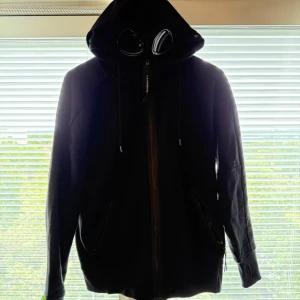 Svart C.P. Company hoodie  - Svart hoodie från C.P. Company, köpt på Nk i Göteborg för ca ett halvår sen men har nästan aldrig använt. Storlek S
