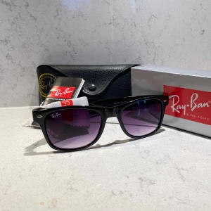 Svarta Ray-Ban Wayfarer solglasögon - Snygga svarta Ray-Ban Wayfarer solglasögon med klassisk fyrkantig form och lila tonade glas. Kommer med originalfodral, putsduk och Ray-Ban booklet. Perfekta för dig som vill ha en ikonisk och tidlös look med en modern twist. Hör av dig vid minsta lilla fundering!