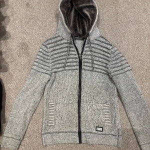 Grå stickad cardigan  - Snygg gråmelerad stickad cardigan från Much More. Med päls i luvan riktigt skön att ha på sig.