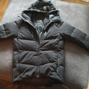 svart sail racing jacka - Säljer en svart pufferjacka från Sail Racing med huva och dragkedja. Jackan har en stilren look med diskret logga på huvan och två bröstfickor med dragkedja. Perfekt för kalla dagar när du vill hålla värmen och ändå se snygg ut.  Ny pris 4500kr endast använd en vinter