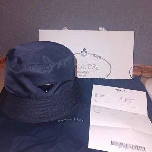 Prada Hatt - Tja, säljer då min Prada Hatt som är i färgen (Mörk Blå). Den är i väldigt väldigt god skick, har användt den på vissa lägen max 10 gånger. Väldigt fräsch och inga problem med den.   Säljer den då jag inte längre har användning för Hatten. Självklart (ÄKTA). Finns kvitto på Hatten så som ni ser.   Vid en snabb och smidig affär skulle jag kunna tänka mig gå ner i någon 100 lapp, så det är bara att slå en pling.   MVH....