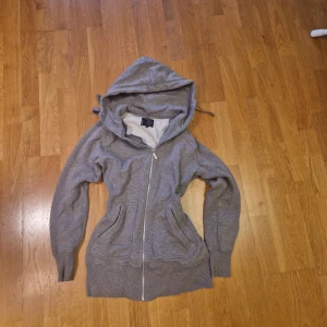 Grå hoodie med dragkedja från Warp - Mysig grå hoodie från Warp med hel dragkedja, huva med snörning och två stora fickor framtill. Insidan är fodrad med mjukt material som känns extra skönt. Perfekt för kyliga dagar och chill vibes.