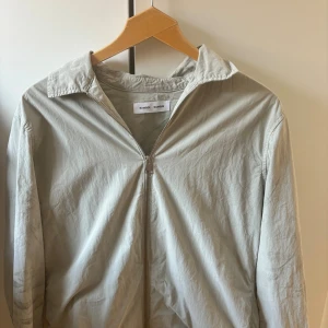 Ljusgrå vindjacka från Samsøe  - Snygg ljusgrå vindjacka från Samsøe Samsøe med klassisk krage och hel dragkedja framtill. Jackan är tillverkad i ett tunt material, perfekt för vår och sommar. 