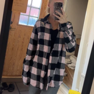 Oversized flanellskjorta - Säljer en oversized flanellskjorta med stora rutor i rosa, svart och grått. Skjortan har klassisk krage, knäppning framtill och två bröstfickor. Perfekt att slänga över en t-shirt för en chill look. Materialet känns mjukt och skönt mot huden.