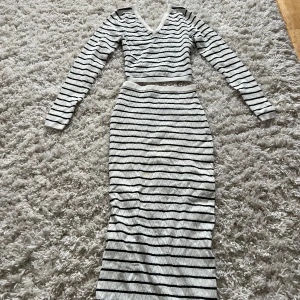 Vit tvådelad outfit/set med svarta ränder - Snygg tvådelad outfit/set  i vitt med svarta horisontella ränder och diskret mönster. Klänningen har lång ärm och v-ringad hals. Materialet är stickat och känns mjukt mot huden. Perfekt för dig som gillar en stilren och modern look.