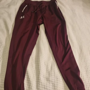 Vinröda mjukisbyxor från Under Armour - Vinröda mjukisbyxor från Under Armour med dragsko i midjan och vita dragkedjor på fickorna. Inga byten. Se gärna mina andra annonser och skapa bundels.