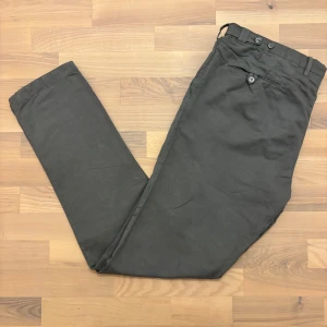 Gråa chinos i linne från Rose & Born - Snygga gråa linnechinos från Rose & Born i samarbete med PT01. Byxorna har raka ben och en klassisk passform med bälteshällor, knappstängning och bakficka med knapp. Tillverkade i en lätt och luftig blandning av 53% linne och 47% bomull, perfekt för varma dagar eller avslappnad stil.  Storlek: 56 Mått: 	•	Midja: 58 cm 	•	Längd: 115 cm 	•	Bredd längst ned: 18 cm 	•	Inseam gylf: 27 cm