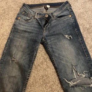 Jeans med slitningar - Mörkblå, lågmidjade jeans med slitningar från HM! Är i fint skick men har lite defekt nere vid fötterna då de slitits upp. Passar mig i längden som är 175! Rekommenderar om ni gillar bootcut Lågmidjade! Skriv om ni har frågor! Pris går att diskutera❤️
