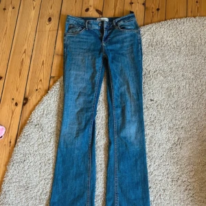 Blå bootcut jeans från Zara - Snygga blå jeans från Zara i klassisk bootcut-modell. Jeansen har normal midja, fem fickor och är tillverkade i ett mjukt denimtyg. Perfekta för dig som gillar en tidlös look med lite utsvängda ben. Midjemåttet: 38cm  Innerbenslängden: 78cm