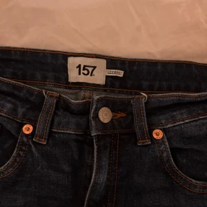 Mörkblå bootcut jeans 157, S short - Mörkblå jeans från 157 med bootcut-modell och låg midja. Klassisk femficksdesign, orange kontrastsömmar och knappstängning framtill. Jeansen är i kraftigt denimtyg och har en snygg, tidlös look som passar till det mesta. Skickar såklart bilder på ifall det skulle önskas. 