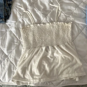 Vit smockad linnetopp Vero Moda XS - Supersöt vit linnetopp från Vero Moda i storlek XS. Toppen har smockad överdel, tunna axelband med knyt och en lätt utställd nederdel. Perfekt för varma dagar och enkel att styla med jeans eller kjol.