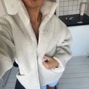 Oversized teddyjacka i ljus beige - Supermysig oversized teddyjacka i ljus beige med hög krage och dragkedja framtill. Jackan har stora fickor och är tillverkad i fluffigt fleece-material. Nypris 1000 kr ungefär