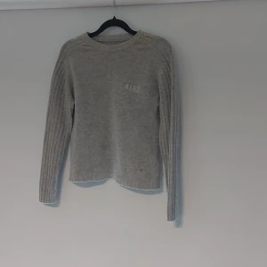 Grå stickad tröja från HERO by Wrangler - Mysig grå stickad tröja från HERO by Wrangler i storlek S. Tröjan har rund halsringning, ribbade långärmar och diskret broderad logga på bröstet. Perfekt för lager-på-lager och chill dagar.