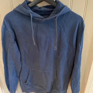 Blå hoodie i ekologisk bomull XS - Mysig blå hoodie från C i ekologisk bomull. Tröjan har huva med snörning, känguruficka framtill och långa ärmar. Perfekt för chill dagar eller när du vill ha något bekvämt och stilrent.