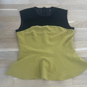 Gul och svart peplumtop från H&M - Snygg peplumtop från H&M i storlek 44. Toppen har en svart mesh upptill och en gul, strukturerad nederdel med markerad midja och volangkant. Stängs med dragkedja bak. Perfekt för dig som vill sticka ut lite extra.
