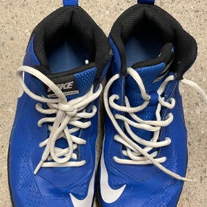 Blåa Nike sneakers med vit sula - Snygga blåa Nike sneakers med vita detaljer och svart foder. Skorna har vit snörning och en robust, mönstrad sula för bra grepp. Perfekta för dig som gillar sportig stil och vill sticka ut med färg. Klassisk Nike-logga på sidan och plös.