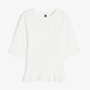 Vit blus med smock och volang - Superfin vit blus med smockad midja och volangkant nertill. Blusen har rund halsringning och halvlånga ärmar, perfekt för en fräsch och stilren look. Tillverkad i mjukt tyg som känns skönt mot huden.