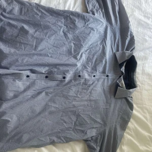 Mönstrad blå skjorta från Morgan - Snygg blå skjorta från Morgan med små cirkelmönster och klassisk krage. Skjortan har långa ärmar, knappar framtill och är tillverkad i stretchigt material för extra komfort. Perfekt för dig som gillar stilrena detaljer och vill ha en skjorta som sticker ut lite.