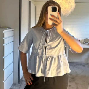 Ljusblå blus med knyte  - Supersöt ljusblå blus från H&M med korta ärmar och volang nedtill. Den är ny med prislapp