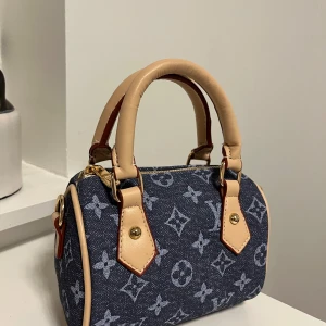 denim handväska - Säljer en snygg liten handväska i blå denim med klassiskt monogrammönster. Väskan har ljusa skinnhandtag, guldiga metalldetaljer och dragkedja upptill. Perfekt storlek för det viktigaste och en riktigt trendig accessoar.