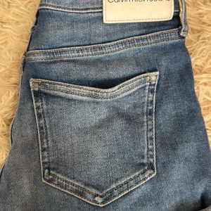 Blå jeansshorts från Calvin Klein - Snygga blå jeansshorts från Calvin Klein med klassisk femficksdesign, uppvikta benslut och logga på bakfickan. Jeansen har en normal passform och är tillverkade i mjukt bomullsjeansmaterial. Perfekta för en avslappnad och trendig look.