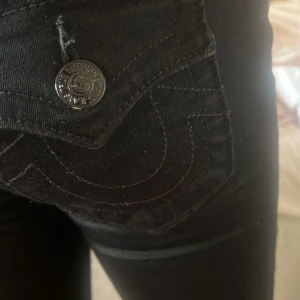 Svarta boot cut  jeans från True Religion - Säljer ett par svarta low bootcut  jeans från True Religion med klassiska bakfickor och tydliga sömmar. Jeansen har låg midja, smal passform och är tillverkade i stretchigt bomullsmaterial. Perfekta för dig som gillar en snygg och stilren look. Köpta för 1299 säljer för 800 de är mid rise men de sitter som low waist på💓