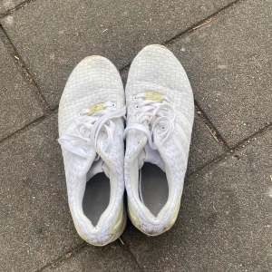 Vita Adidas sneakers herr strl 42 - Snygga vita Adidas sneakers med vävt mönster och detaljer i syntet. Skorna har snörning, rund tå och platt sula. Perfekta för dig som gillar stilrena och sportiga vibes. Adidas logga på plösen och stabil hälkappa.