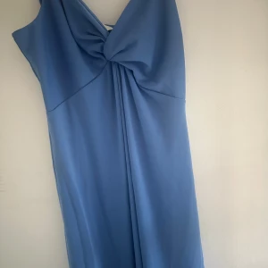 Blå långklänning från H&M med rosett - Snygg blå långklänning från H&M i storlek S. Klänningen har en stor rosettdetalj framtill och smockad rygg för extra komfort. Materialet är mjukt och lätt, perfekt för varma dagar. Stilren och enkel design med axelbandslös passform. Tar frakt!