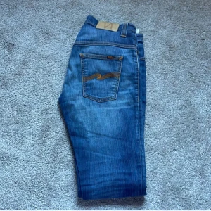 Blå Nudie jeans Nyskick - Skriv vid frågor och funderingar. Säljer ett par klassiska blå jeans från Nudie Jeans Co med snygga kontrastsömmar och ikonisk broderad bakficka. Jeansen är nästan helt nya och är 10/10 i skick säljer dessa då den var för stora för mig när jag köpte de för nån månad sen!