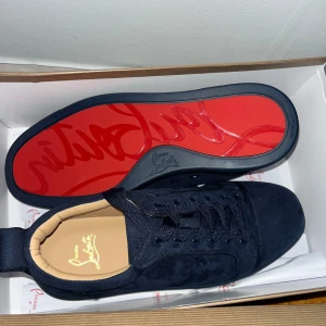 Mörkblå sneakers från Christian Louboutin - Snygga mörkblå sneakers från Christian Louboutin i mocka med klassisk röd sula och diskret logga på sidan. Skorna har rund tå, platt sula och snörning. Perfekta för dig som vill sticka ut med exklusiv stil och detaljer.